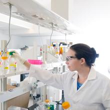 Student wearing safety glasses reaching for chemical on shelf